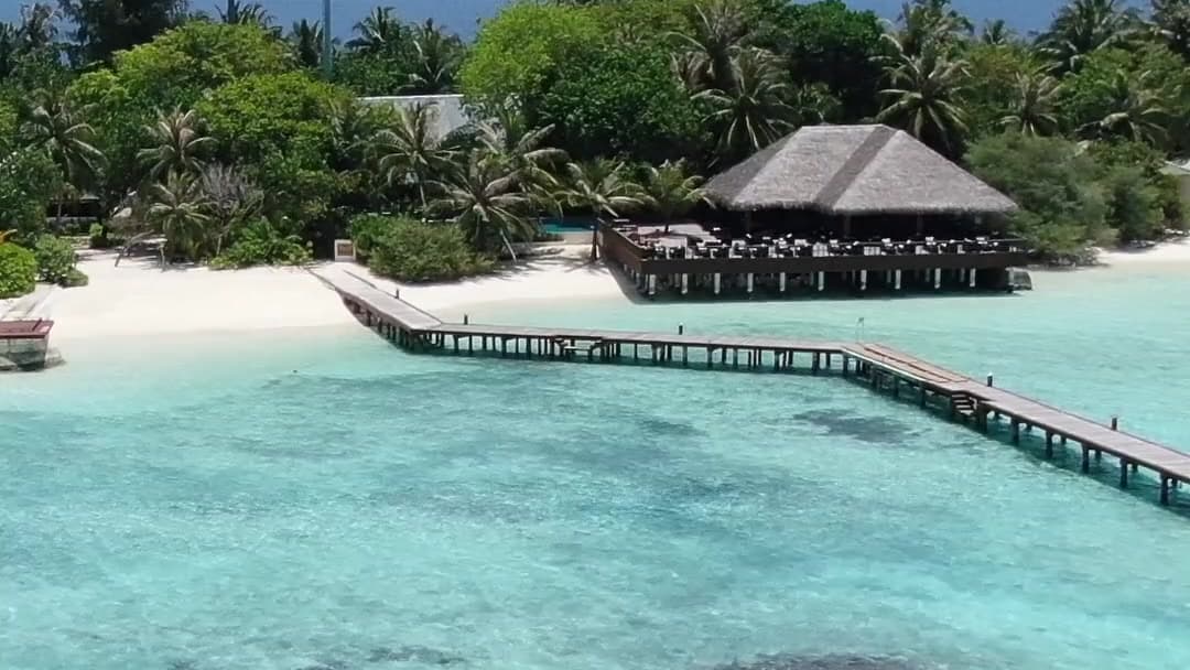 A Maldives resort island and its jetty above the coral reef, seen from a drone